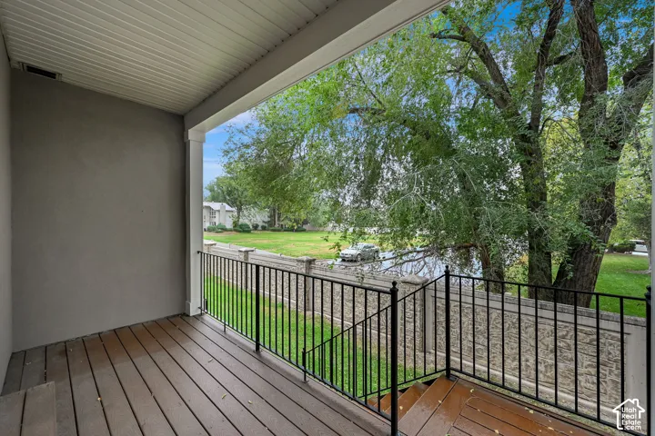 Covered porch featuring wood-finish decking, black metal railing, and staircase with access to a fenced outdoor area