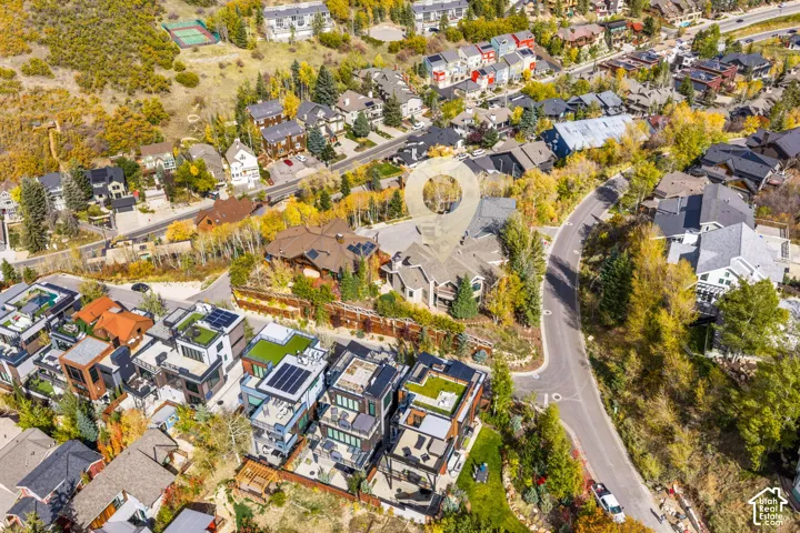 Aerial perspective of a multi-level residential development featuring rooftop terraces, solar panel arrays, and paved street access within a forested mountain setting