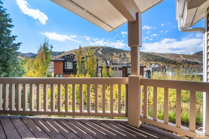 Covered deck with wooden decking, painted wood-slat railing, and overhead structural support, featuring a mountain backdrop