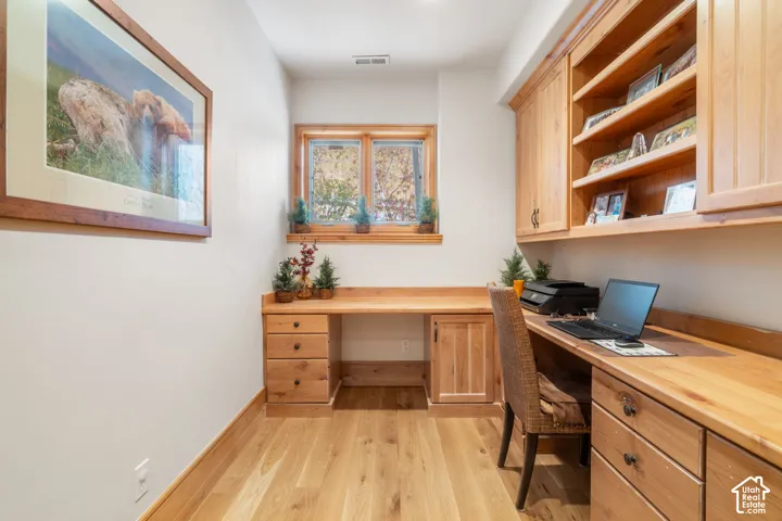 Built-in natural wood cabinetry and desk workspace featuring drawers and open shelving, paired with natural wood-finish flooring
