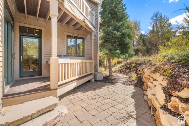Covered deck featuring wood-finish decking and integrated railing, paver patio, and natural stone retaining wall