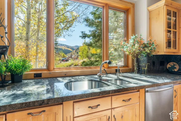 Natural wood cabinetry, stone countertops, stainless steel dual-basin undermount sink, gooseneck faucet, and large picture windows featuring mountain scenery