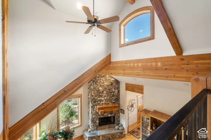 Vaulted ceilings featuring exposed wood beams, full-height stone fireplace with a thick wood mantel, arched window, and ceiling fan