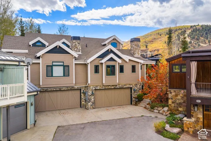 Multi-level residence featuring stone and horizontal siding exterior, dual garage doors, decorative gable rooflines, and mountain backdrop