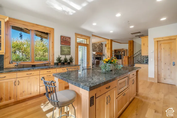 Kitchen featuring natural wood cabinetry, stone countertops, a large center island with built-in microwave, wood-finish flooring, and recessed lighting