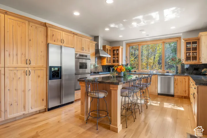 Kitchen featuring natural wood cabinetry, granite countertops, a center island with bar seating, stainless steel appliances, and wood-finish flooring