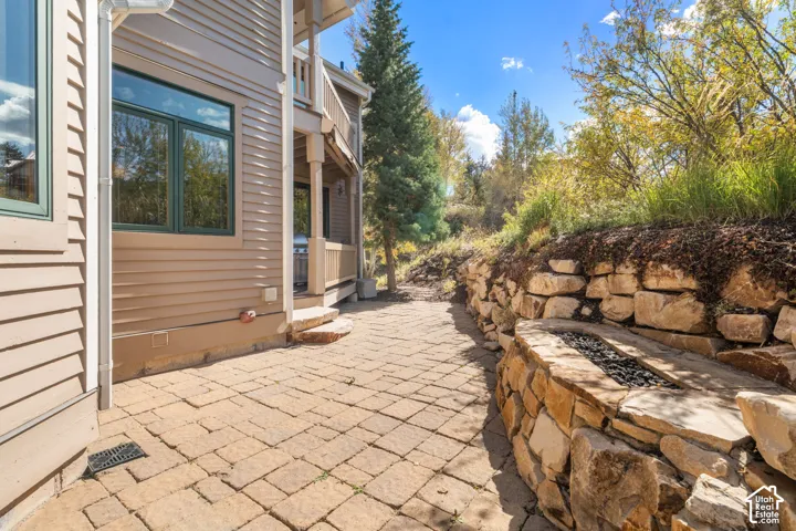Stone-paver patio featuring a natural stone retaining wall and a built-in stone fire pit