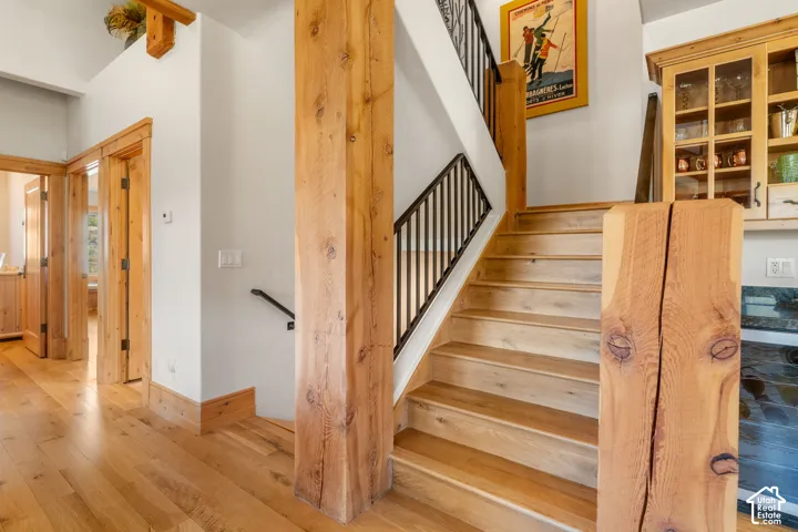Staircase featuring heavy timber support posts, wood-finish treads, and wrought-iron balusters, complemented by wood-finish door casings and built-in glass-front cabinetry