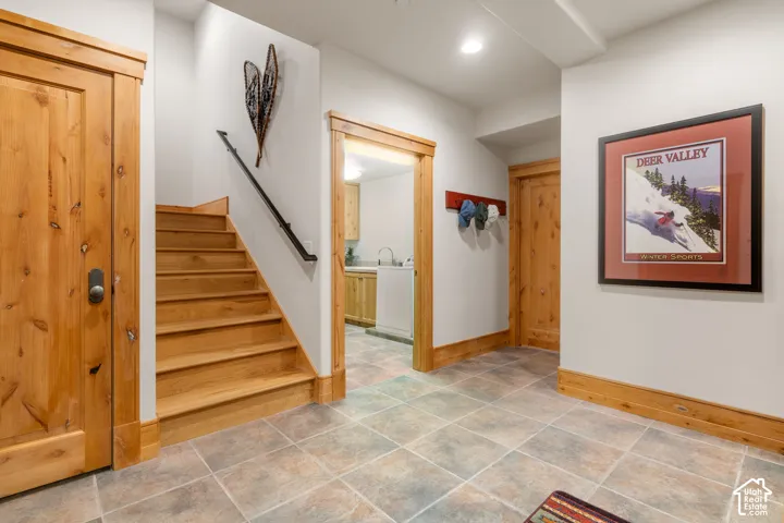Entryway featuring tile flooring, natural wood-trimmed doors and millwork, staircase with a matte black handrail, and recessed lighting