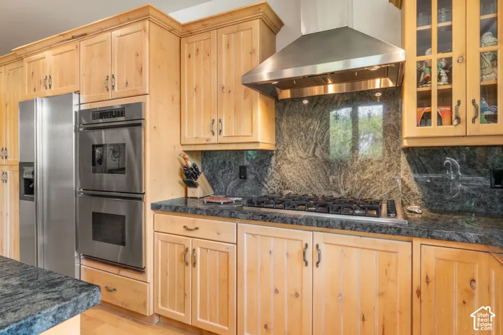 Kitchen featuring custom natural wood cabinetry, stone countertops, integrated backsplash, stainless steel double wall oven, and a stainless steel range hood