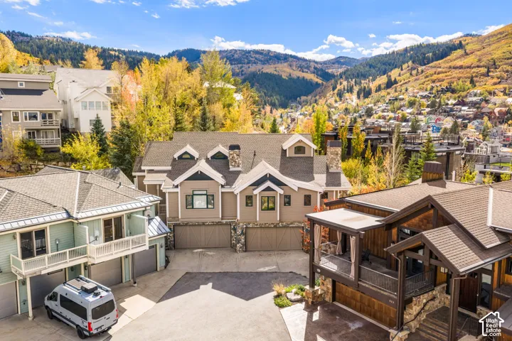 Mountainous landscape backdrop with multi-story residential architecture, gabled rooflines, stone masonry accents, and multi-car garage configuration