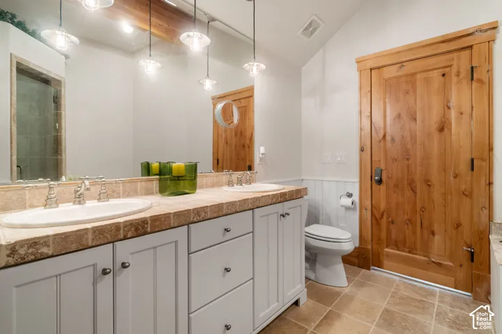 Spa-inspired primary bathroom featuring dual vanities with stone countertops, soft-close cabinetry in white finish, pendant lighting, and tile flooring