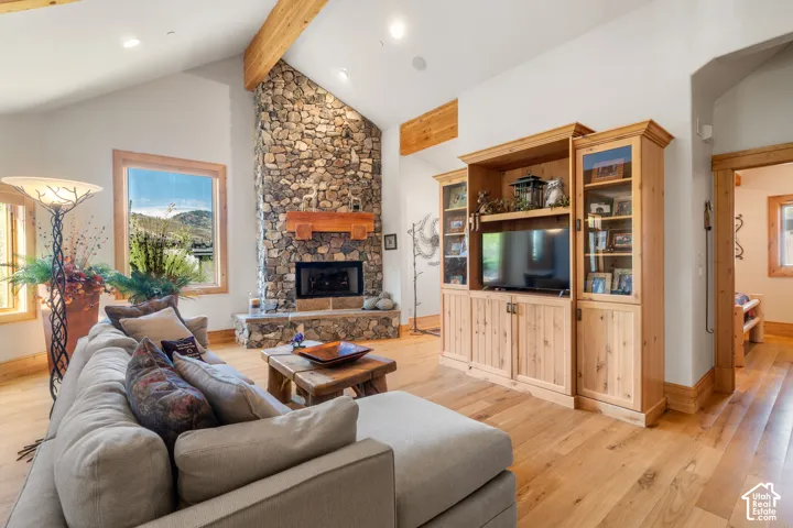 Vaulted ceilings with exposed timber beams, floor-to-ceiling stone fireplace with a thick wood mantel, built-in light-wood cabinetry, and wood-finish flooring