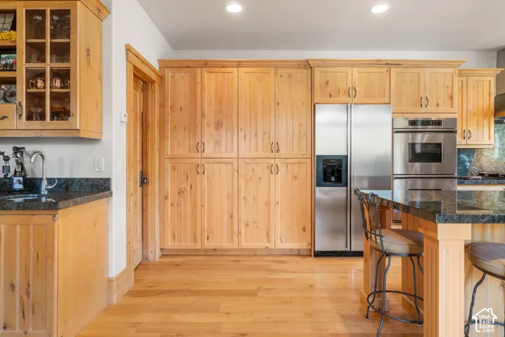 Kitchen featuring custom natural wood cabinetry, dark stone countertops, wood-finish flooring, and built-in stainless steel appliances including a double wall oven and French door refrigerator