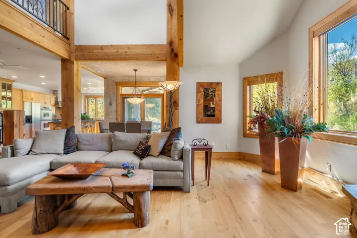 Vaulted ceilings featuring exposed timber beams, wood-finish flooring, extensive natural light through large windows, and an interior balcony with a metal railing