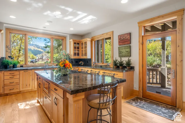 Kitchen featuring natural wood cabinetry, dark stone countertops, wood-finish flooring, a center island, and a glass-paneled exterior door
