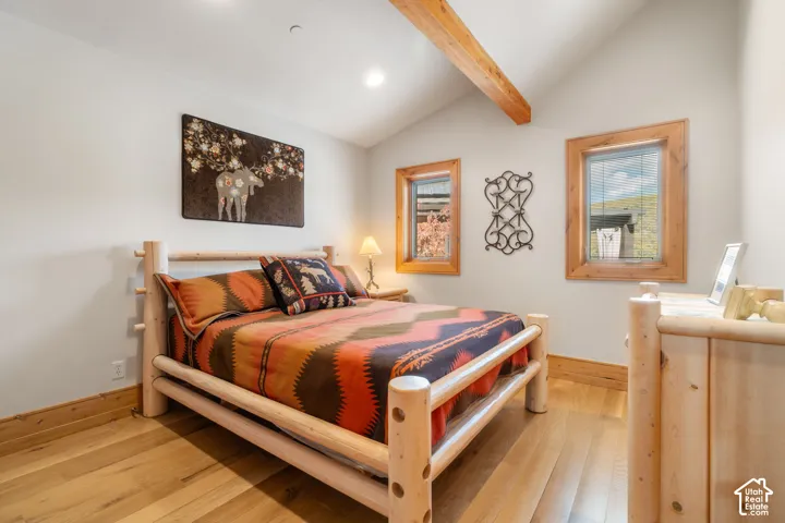 Vaulted ceiling featuring an exposed wood beam, natural wood-finish flooring, and wooden window trim