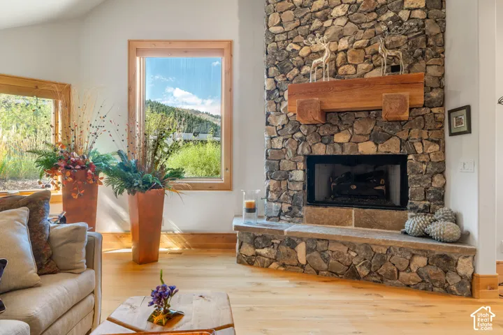 Floor-to-ceiling stone fireplace featuring a heavy timber mantel and raised stone hearth, complemented by wood-finish flooring and expansive windows with natural mountain scenery