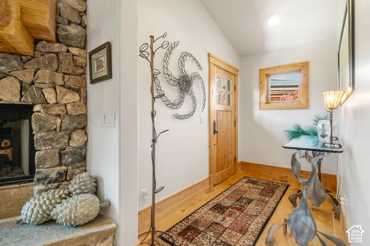 Fireplace featuring a floor-to-ceiling stone surround, light-toned wood-finish flooring, natural wood trim, and a solid wood entry door with glass inserts