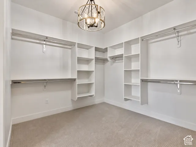 Primary Bedroom walk-in closet featuring white custom built-in shelving, multi-level metal hanging rods, neutral carpeting.