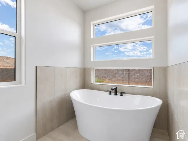 Primary Bathroom with freestanding white soaking tub featuring a matte black deck-mounted faucet, surrounded by neutral-toned tile wall treatments and stacked transom windows