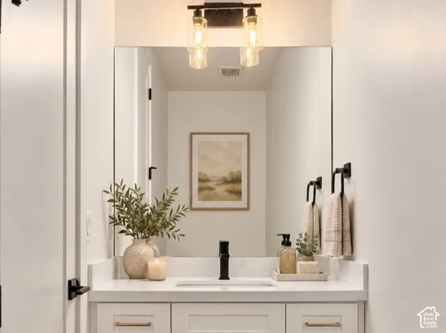 Half bath w/white vanity featuring a solid surface countertop, rectangular under-mount sink, matte black faucet, and metallic hardware, complemented by a large wall-mounted mirror and two-light fixture. Home is virtually staged.