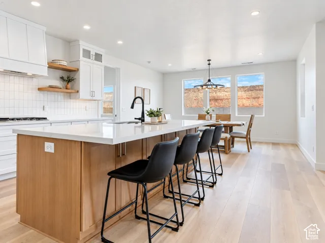 Kitchen featuring a wood-finish island with a white countertop, white cabinetry with integrated floating shelving, a subway tile backsplash, and light-toned wood-finish flooring