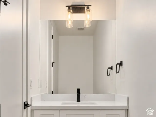 Half bath w/white shaker-style vanity with a stone countertop, rectangular undermount sink, matte black hardware, and large rectangular mirror featuring a dual-bulb vanity light