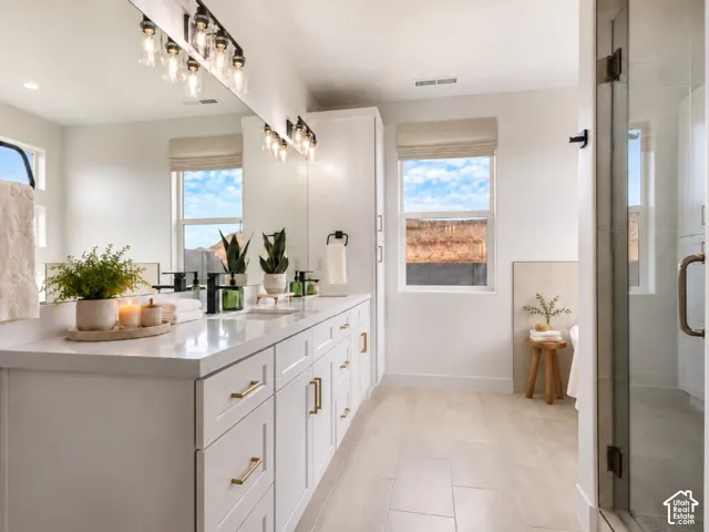 Primary Bathroom with double vanity with white cabinetry, quartz countertops, dual undermount sinks, complemented by large-format floor tiling and a glass-enclosed shower