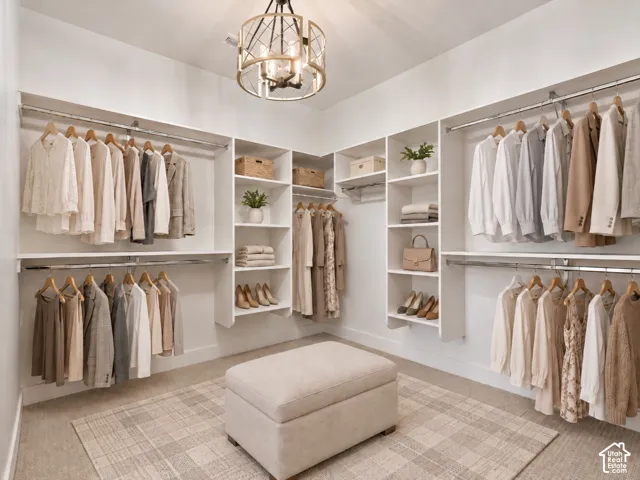 Primary Bedroom walk-in closet featuring extensive built-in white shelving, tiered hanging rods, carpeted flooring, and a decorative chandelier. Home is virtually staged.