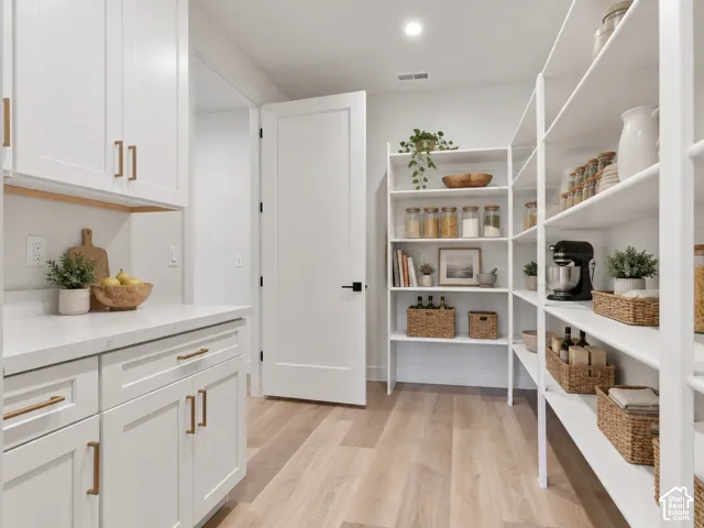 Walk-in pantry featuring wood-finish flooring, custom white cabinetry, light-toned quartz countertops, and open white shelving. Home is virtually staged