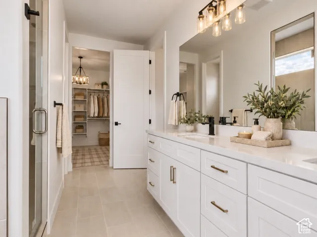 Double vanity featuring white cabinetry, quartz countertops, hardware, and an expansive wall mirror with overhead light fixtures leads to walk in closet. Home is virtually staged.