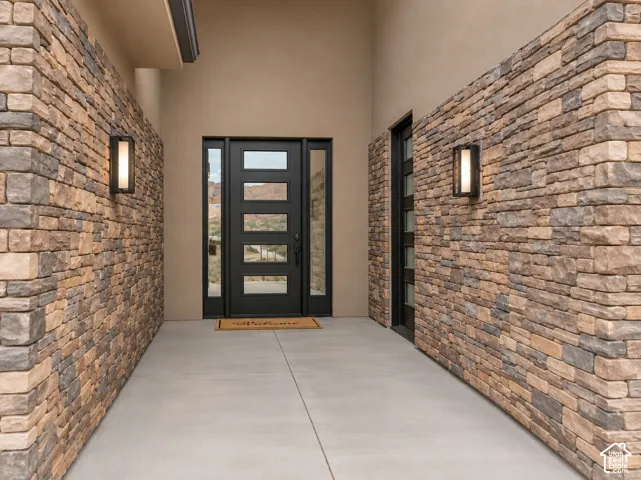 Covered entryway featuring natural stone veneer walls, a modern multi-lite door with side panels, and rectangular wall-mounted exterior light fixtures