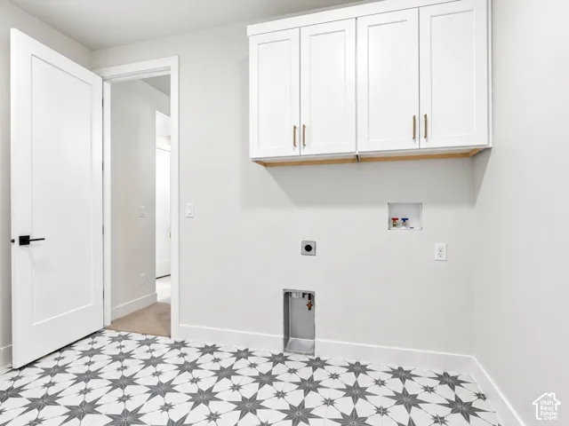 Laundry room featuring patterned tile flooring, white shaker-style wall cabinetry with metallic pulls, washer/dryer hookups