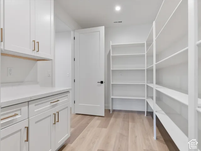Walk-in pantry featuring white shaker-style cabinetry, solid-surface countertops, metallic hardware, wood-finish flooring, and integrated wall shelving