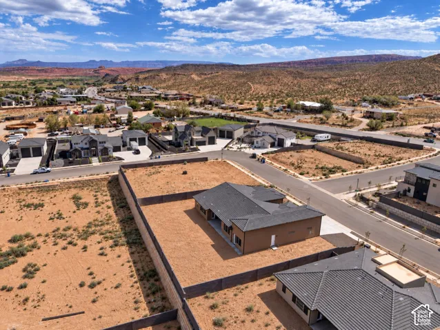 Aerial perspective of a detached single-story residence featuring a tile roof, an expansive perimeter wall, and a large fenced lot with mountain horizon surroundings