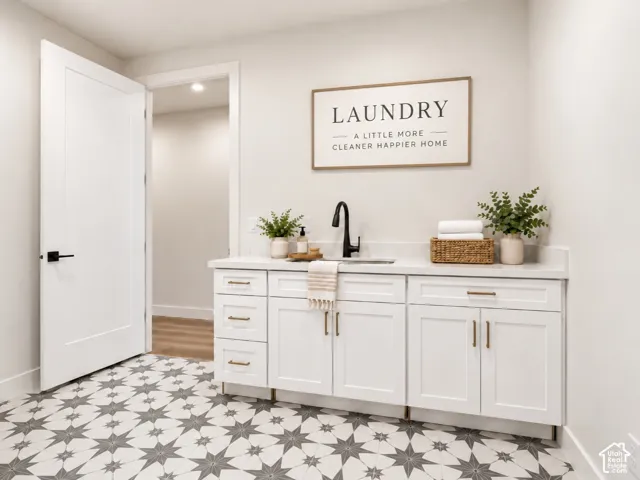 Laundry room featuring white shaker-style cabinetry, quartz countertop, inset sink with geometric patterned tile flooring. Home is virtually staged
