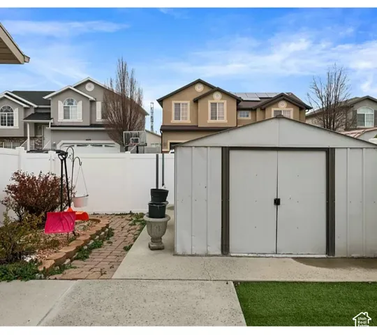 Backyard featuring a white vinyl privacy fence, metal storage shed, concrete patio, and segmental retaining wall
