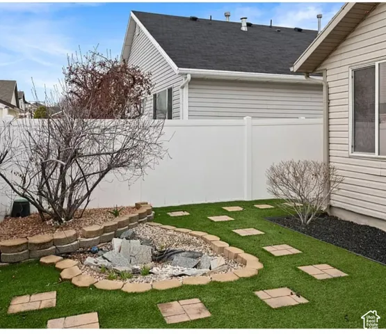 Backyard featuring synthetic turf, decorative stone-bordered garden beds, a stone water feature, and a privacy fence