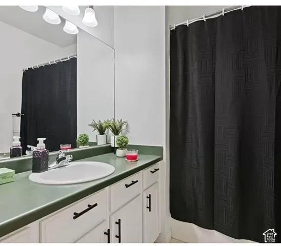White cabinetry featuring matte black hardware, solid-surface countertop with an integrated oval sink, full-width mirror, and four-light vanity fixture