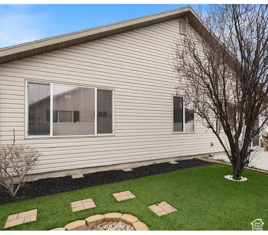 Exterior featuring horizontal vinyl siding, multi-pane windows, synthetic turf, stone-bordered fire pit, and stone pavers