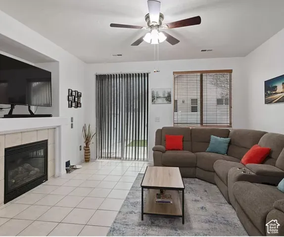 Living area featuring a tile-surround fireplace, built-in shelving, vertical blinds, and a ceiling fan with integrated lighting