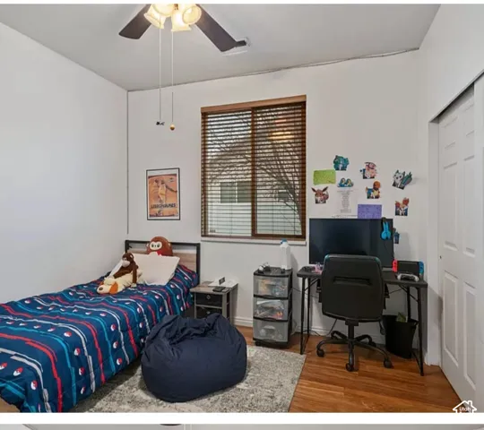 Room featuring wood-finish flooring, a window with horizontal slat blinds, a ceiling fan with integrated lighting, and a sliding-door closet