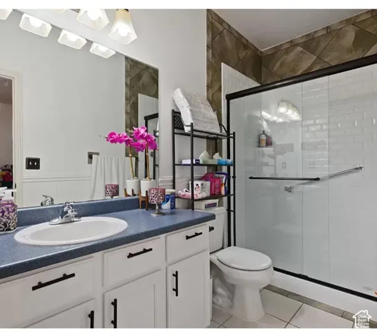 White vanity featuring matte black hardware, integrated sink, and solid-surface countertop, paired with a shower enclosure featuring white subway tile, decorative diamond-patterned accent tile, and a sliding glass door