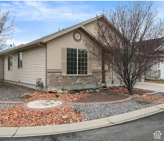 Single-story exterior featuring a combination of horizontal siding and masonry veneer, a gabled roofline, grid-patterned windows with decorative shutters, and xeriscaped grounds with integrated stone borders