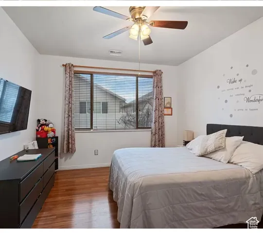Room featuring wood-finish flooring, a ceiling fan with integrated lighting, and a large window with horizontal blinds