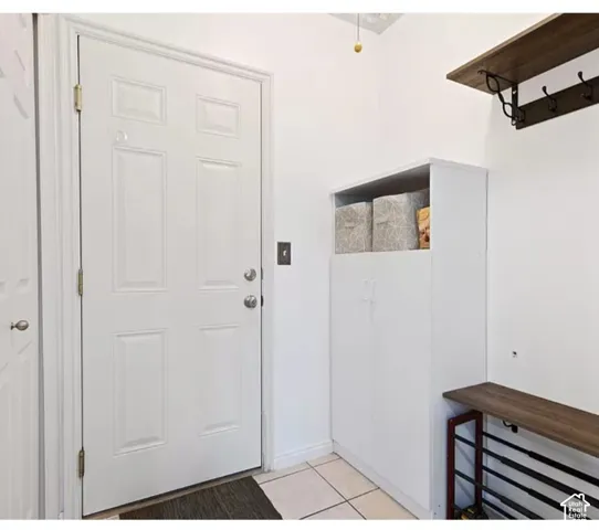 Entryway featuring a six-panel door with a brushed-nickel deadbolt, white built-in cabinetry, wall-mounted dark wood-finish shelving, and tiled flooring