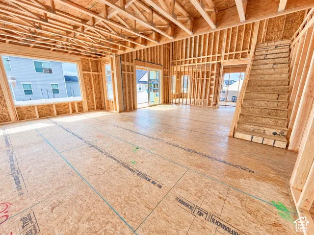Open-concept structural framing featuring exposed wood-truss ceiling, unfinished staircase, large window openings, and glass sliding door