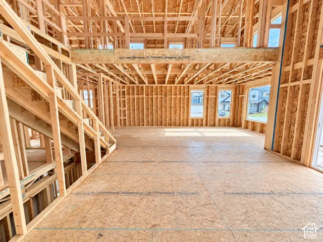 Open-concept structural framing featuring exposed wood wall studs, subfloor decking, high-ceiling rafters, and a staircase framework