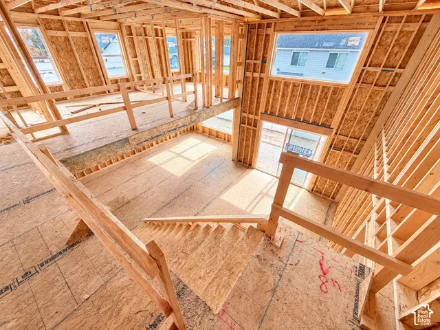 New construction interior framing featuring high-ceiling structural elements, open floor plan design, multiple window openings, and wooden staircase construction